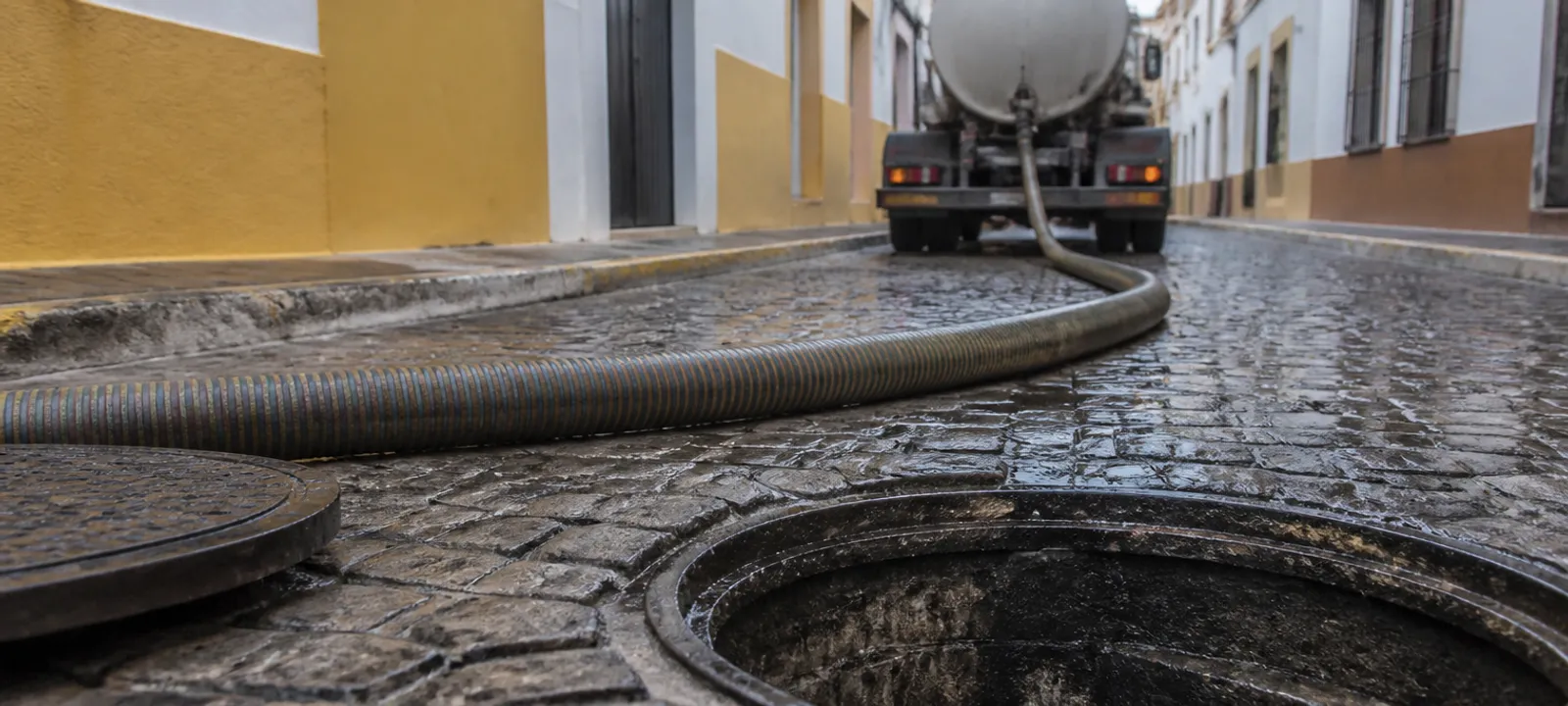 Arqueta abierta y manguera de succión en una calle de Sevilla durante un desatasco de día